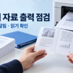 프린터와 파란 폴더 옆에서 출력한 경매 분석자료의 쪽 순서와 모서리를 대조하는 장면